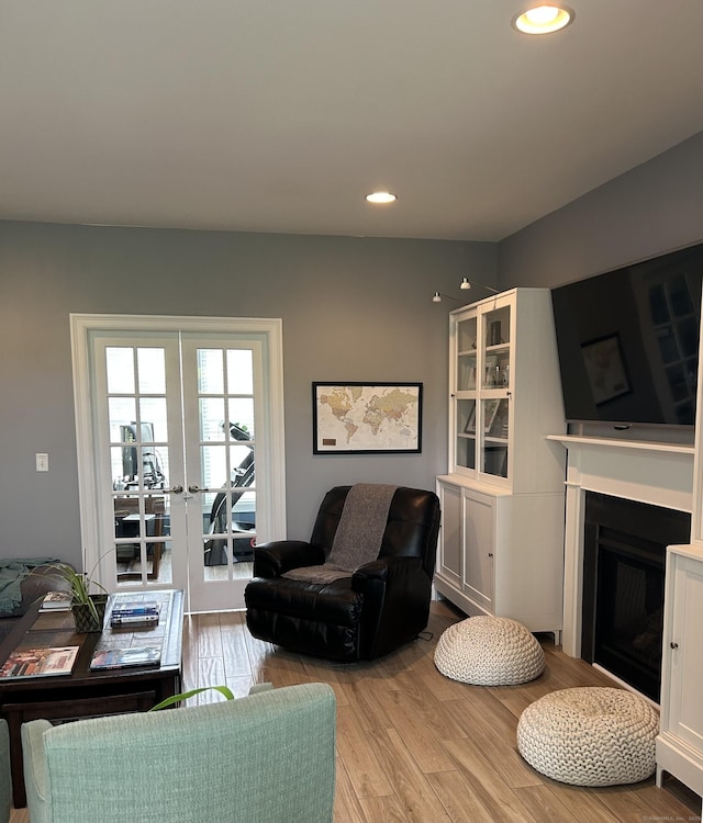 living area featuring light wood-style floors, recessed lighting, a fireplace, and french doors