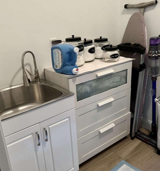 details featuring a sink, wood finished floors, and white cabinetry