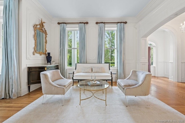 living area with ornamental molding, arched walkways, a decorative wall, and parquet flooring