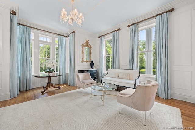 living area featuring light wood-style floors, a notable chandelier, a decorative wall, and crown molding