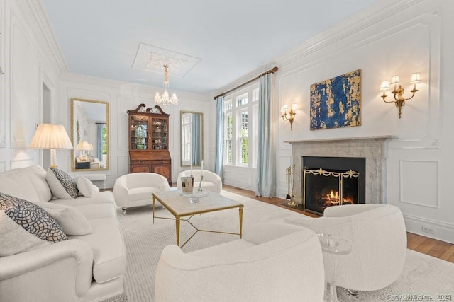 living room with ornamental molding, wood finished floors, a decorative wall, a notable chandelier, and a high end fireplace