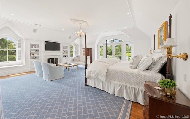 bedroom featuring lofted ceiling, multiple windows, a fireplace, and wood finished floors