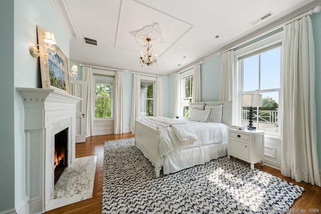 bedroom featuring ornamental molding, dark wood-style flooring, visible vents, and a premium fireplace