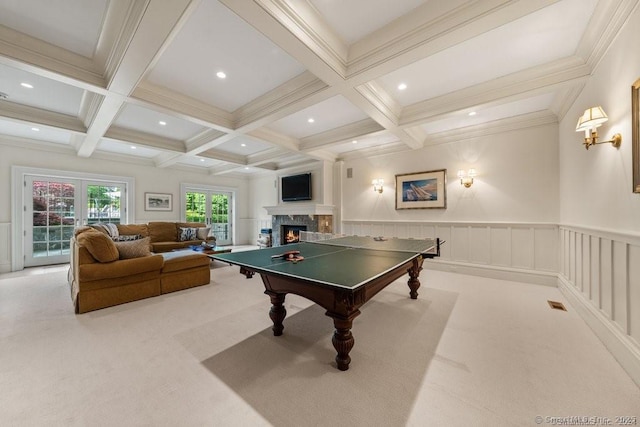 recreation room with coffered ceiling, a warm lit fireplace, light colored carpet, and beamed ceiling