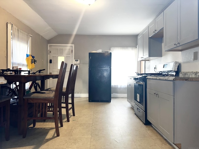 kitchen with baseboards, dark countertops, freestanding refrigerator, vaulted ceiling, and stainless steel range with gas cooktop