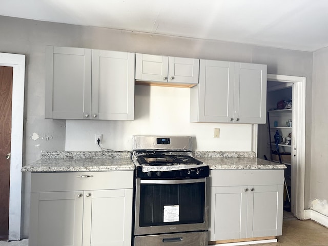 kitchen with light stone counters, stainless steel gas stove, and white cabinetry