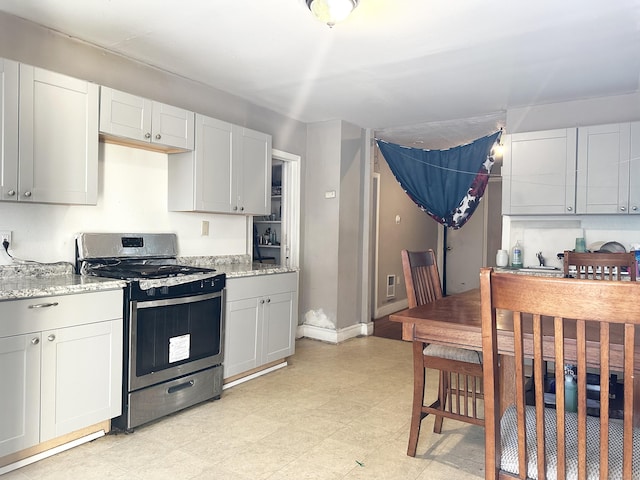 kitchen featuring light stone counters, gas stove, baseboards, and light floors