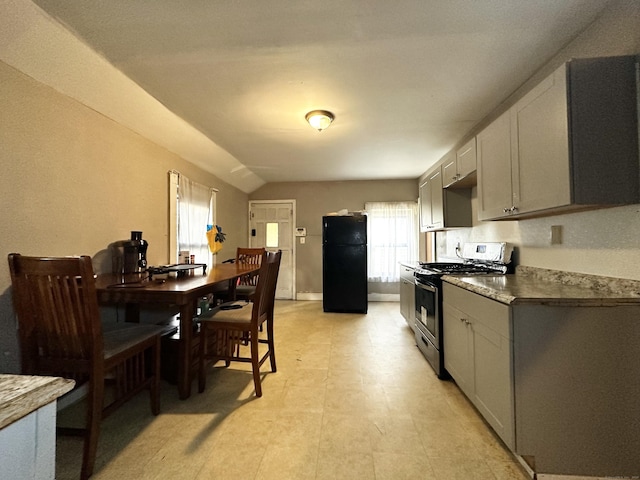 kitchen featuring lofted ceiling, gas stove, freestanding refrigerator, and gray cabinetry