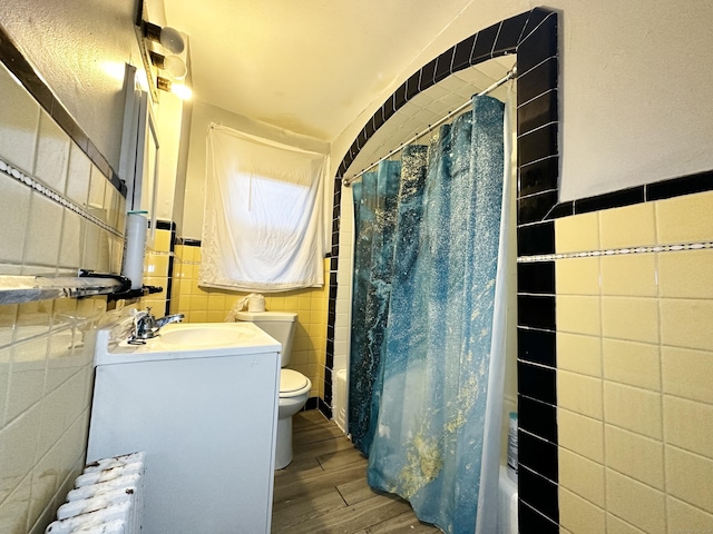 bathroom featuring toilet, shower / tub combo with curtain, tile walls, and wood finished floors