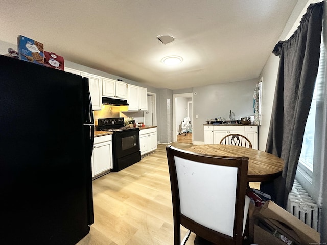 kitchen with radiator, black appliances, under cabinet range hood, and white cabinetry