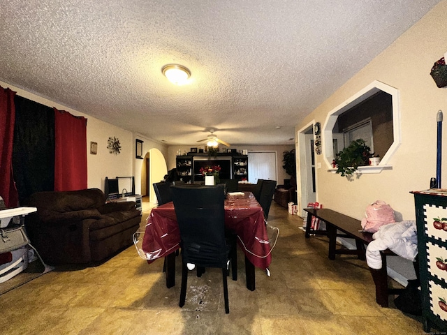 dining area with a textured ceiling, arched walkways, and a ceiling fan