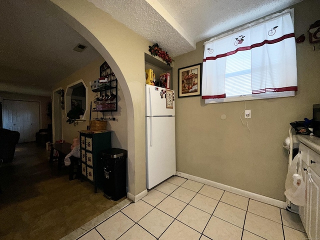 kitchen with light tile patterned floors, visible vents, arched walkways, freestanding refrigerator, and a textured ceiling