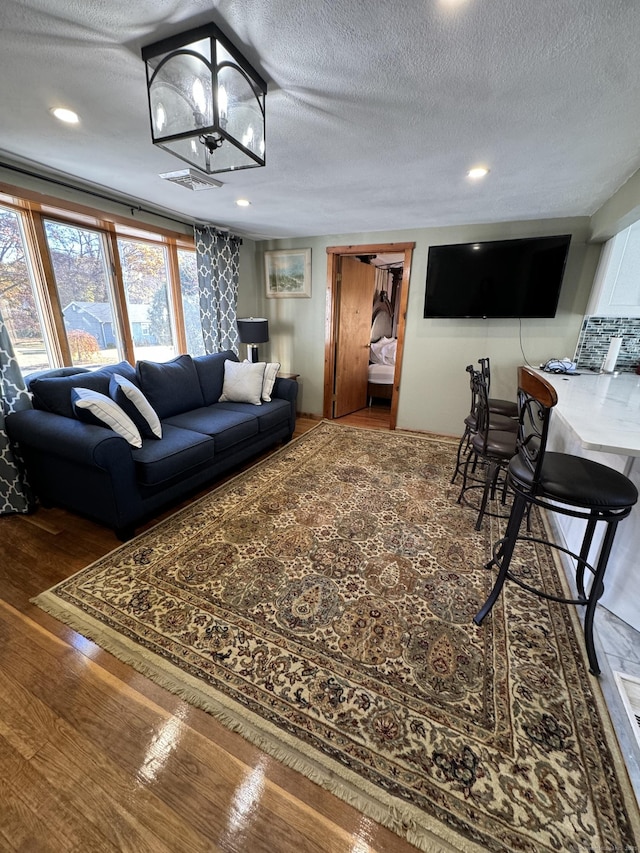 living room featuring an inviting chandelier, a textured ceiling, wood finished floors, and recessed lighting