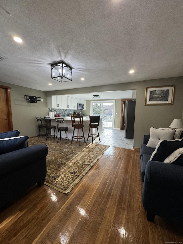 living room featuring light wood-type flooring, visible vents, a textured ceiling, and recessed lighting