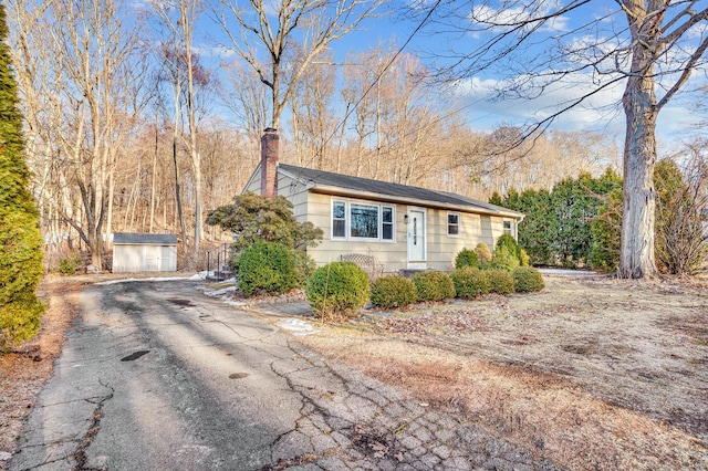 view of front of home with driveway, a chimney, a storage unit, and an outbuilding