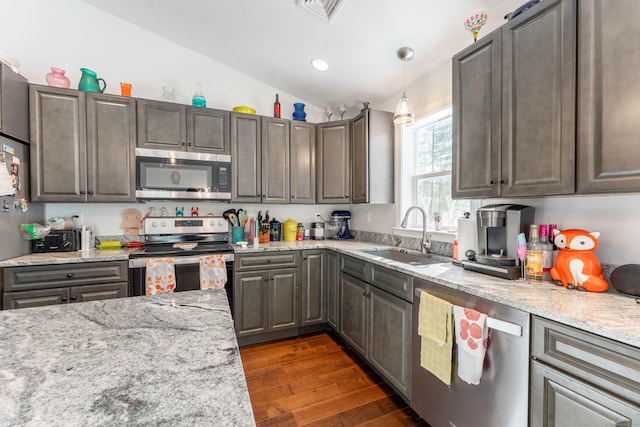 kitchen featuring dark wood-style floors, appliances with stainless steel finishes, decorative light fixtures, vaulted ceiling, and a sink