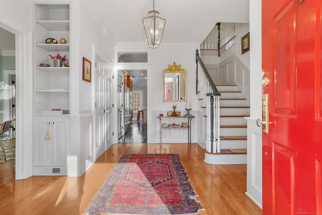 foyer entrance with ornamental molding, a chandelier, stairs, and wood finished floors