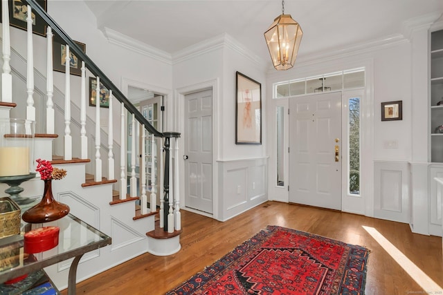 foyer featuring wainscoting, wood finished floors, crown molding, a chandelier, and a decorative wall