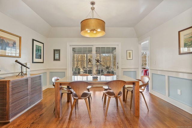 dining room featuring lofted ceiling, a decorative wall, wood finished floors, and wainscoting