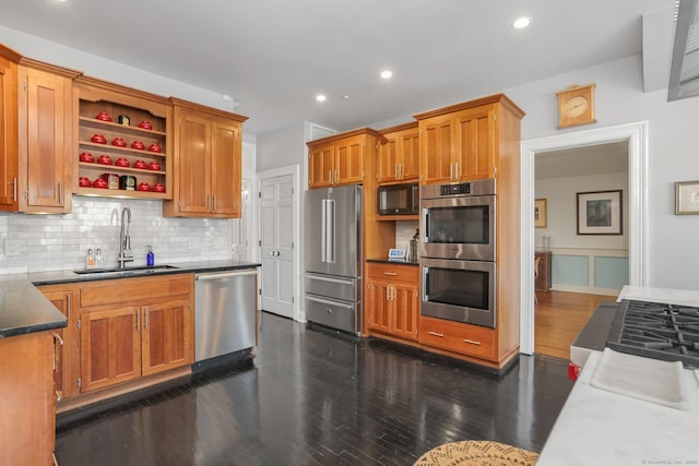 kitchen featuring stainless steel appliances, dark wood-style flooring, a sink, backsplash, and dark countertops