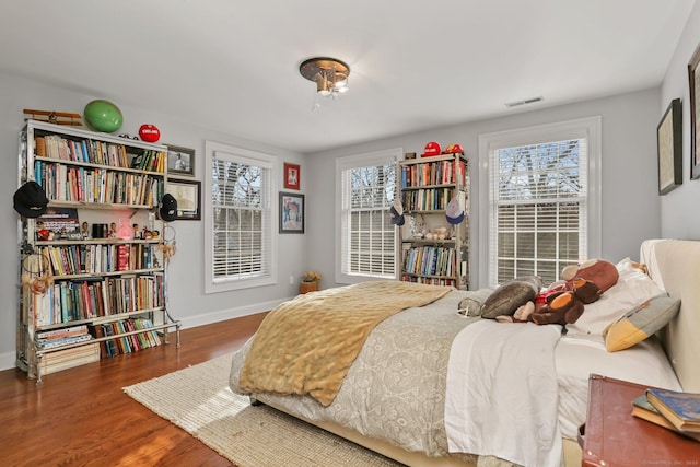 bedroom with multiple windows, wood finished floors, visible vents, and baseboards