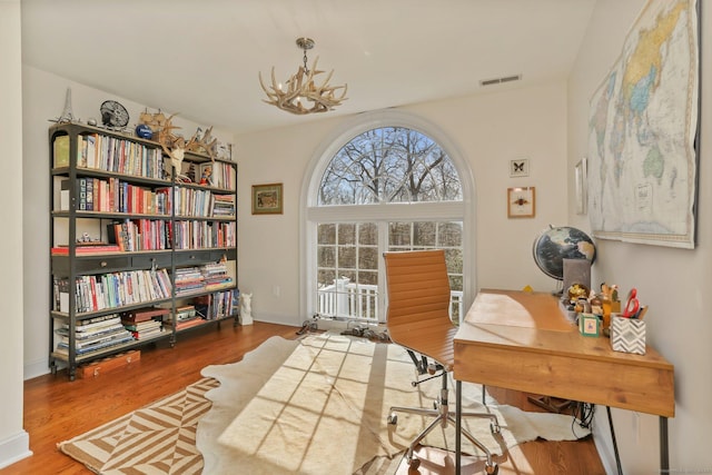 office space featuring an inviting chandelier, baseboards, visible vents, and wood finished floors