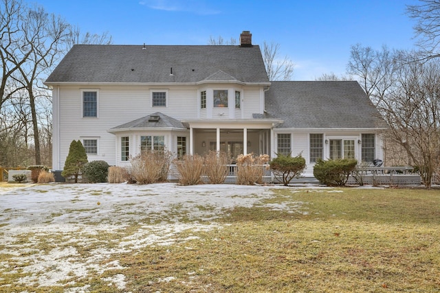 snow covered house featuring a lawn, roof with shingles, a chimney, and a sunroom