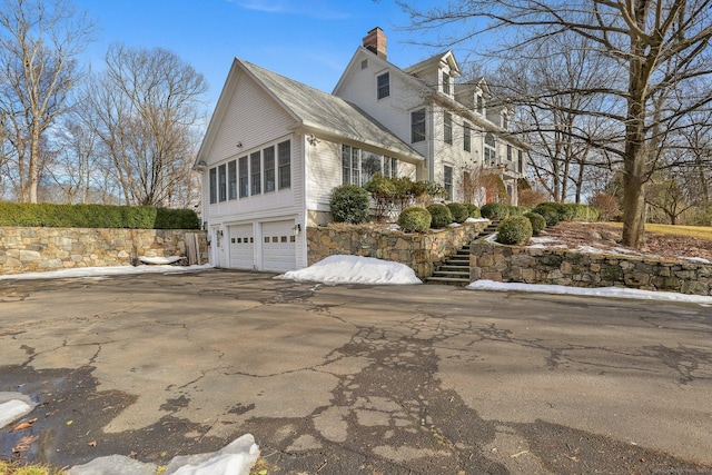 view of side of home featuring a garage, driveway, a chimney, and stairs