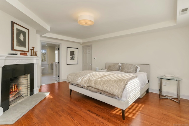 bedroom with a warm lit fireplace, baseboards, visible vents, and wood finished floors