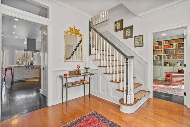 stairway featuring recessed lighting, crown molding, a decorative wall, and wood finished floors