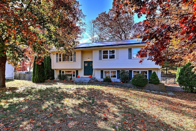 bi-level home with a front yard, roof mounted solar panels, and fence