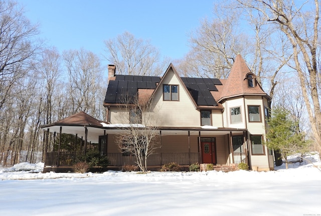 view of front of property with a porch, a chimney, and solar panels