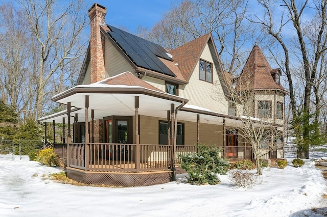 victorian house featuring a chimney, a porch, and solar panels