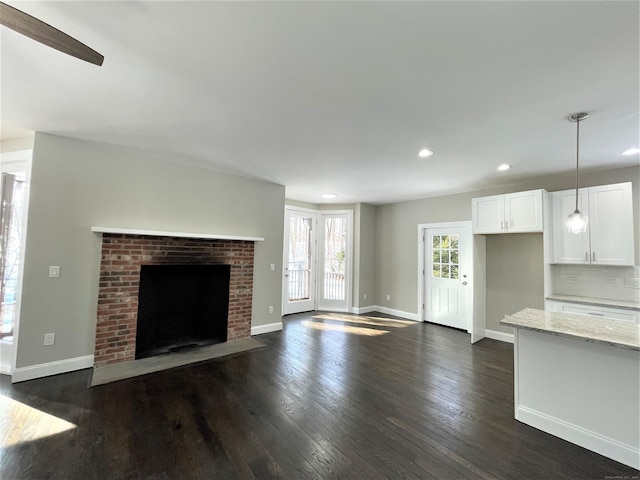 unfurnished living room featuring dark wood-type flooring, recessed lighting, a brick fireplace, and baseboards