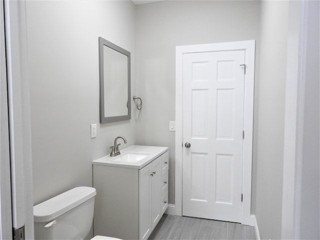 half bathroom featuring vanity, toilet, and baseboards