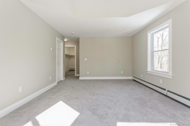 unfurnished bedroom with a baseboard heating unit, a walk in closet, light colored carpet, and baseboards