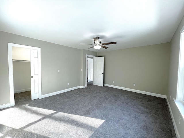 unfurnished bedroom featuring ceiling fan, dark carpet, a walk in closet, and baseboards