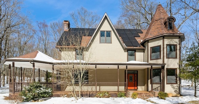 view of front facade with covered porch, a chimney, and solar panels