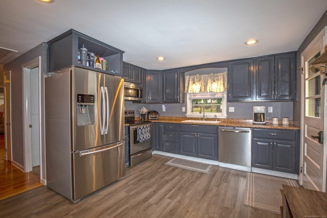 kitchen featuring appliances with stainless steel finishes, dark wood-style flooring, a sink, and light stone countertops