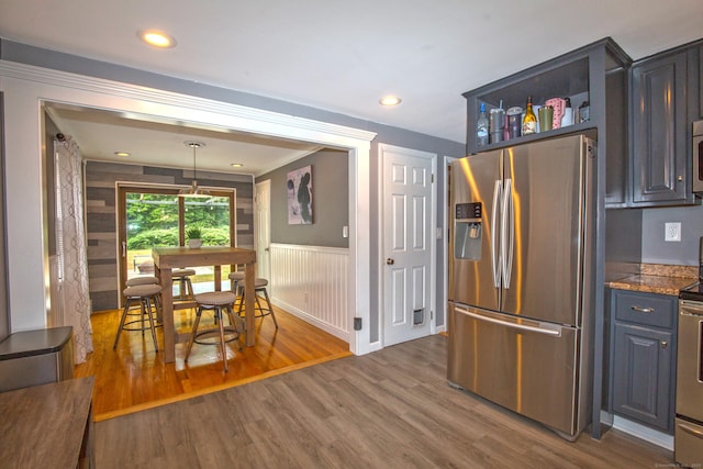 kitchen with stainless steel appliances, dark wood-style flooring, wainscoting, dark stone countertops, and decorative light fixtures