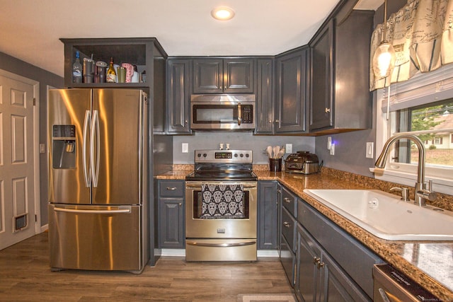 kitchen featuring light stone counters, dark wood-type flooring, a sink, appliances with stainless steel finishes, and pendant lighting