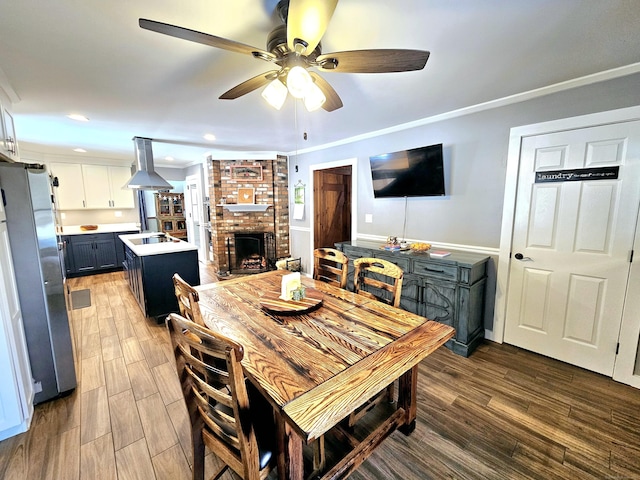 dining room featuring a ceiling fan, ornamental molding, wood finished floors, a fireplace, and recessed lighting