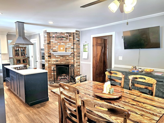 dining space featuring ornamental molding, light wood-type flooring, a fireplace, and a ceiling fan