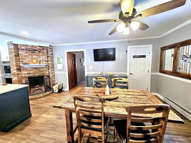 dining space featuring ceiling fan, a baseboard radiator, light wood-style flooring, a fireplace, and ornamental molding