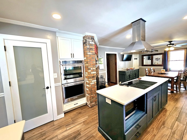 kitchen featuring stainless steel double oven, black electric cooktop, white cabinets, light wood-type flooring, and island exhaust hood