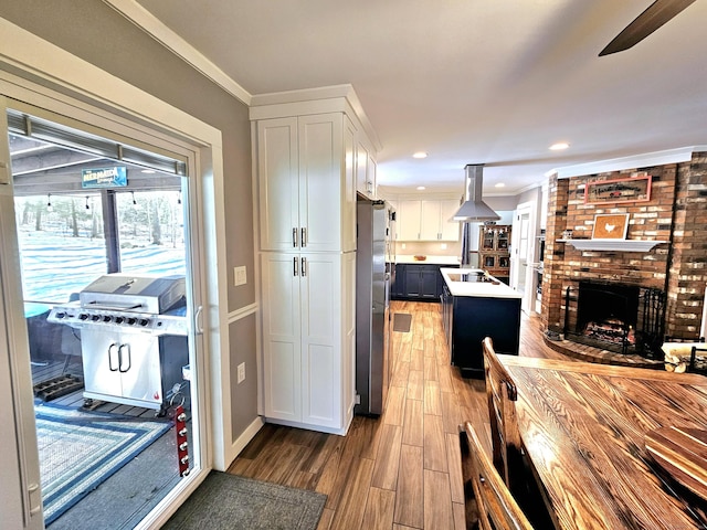 kitchen featuring freestanding refrigerator, a brick fireplace, white cabinets, island range hood, and wood finished floors