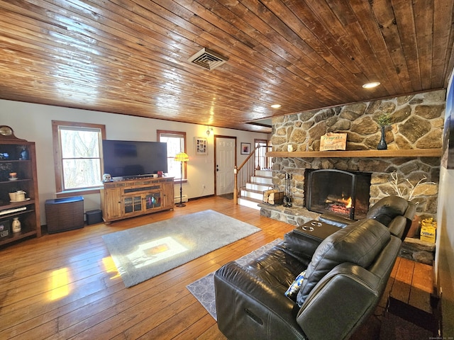 living room featuring a stone fireplace, visible vents, stairway, baseboard heating, and hardwood / wood-style floors