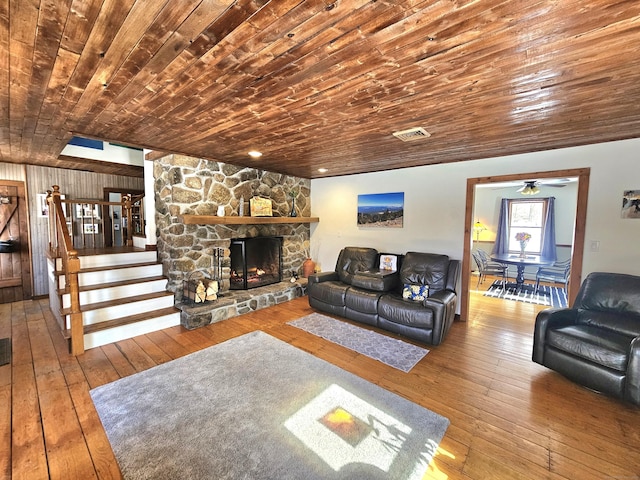 living room with wood-type flooring, visible vents, stairway, and a stone fireplace