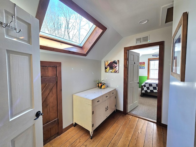 bathroom with hardwood / wood-style flooring, vaulted ceiling with skylight, visible vents, and baseboards