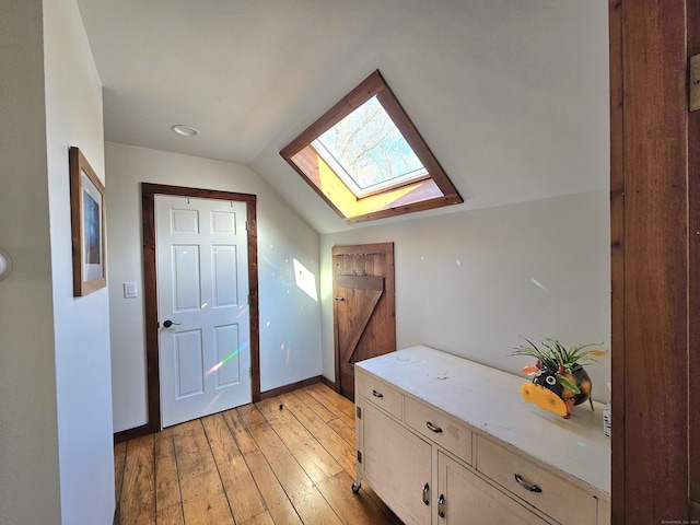 interior space featuring vaulted ceiling with skylight, light wood-type flooring, and baseboards